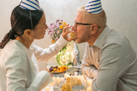 Couple Birthday Cake Celebration: Indoor intimate birthday party, woman feeds man cake, joyful moment.