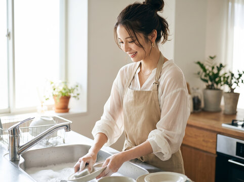 笑顔で楽しそうにお皿を洗うエプロン姿の女性
