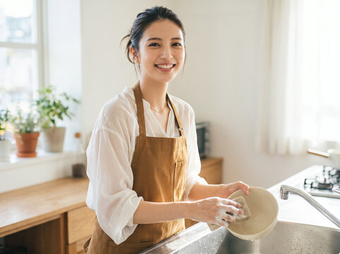 エプロンを着て台所で笑顔で食器を洗う女性