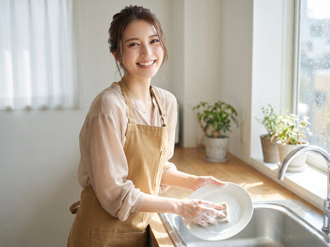 キッチンでエプロンを着けて笑顔で皿を洗う女性