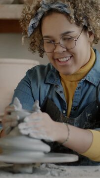Skilled female potter making vase from clay using traditional throwing wheel in workshop. Creative occupation and small business concept.