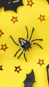 Top view of plastic spider and black bats spinning on yellow background in vertical orientation, Halloween holiday decoration rotating. Spooky seamless background. Halloween backdrop