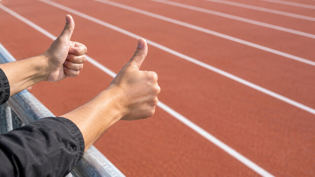 Man showing thumbs up gesture over running track at stadium. Support and approval sign from fan cheering during athletics competition.