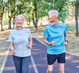 Fototapeta premium Smiling active mature senior couple jogging together in the park
