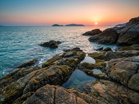 Rocky coastline sunset ocean view with tidal pools and distant islands on the horizon