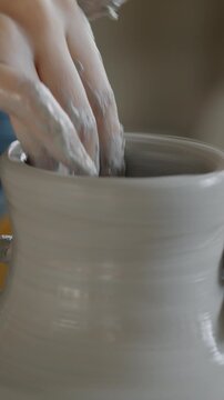 Close-up of potter's hands shaping beautiful vase from wet clay manufacturing vessel in workshop. Manual labor and production concept.