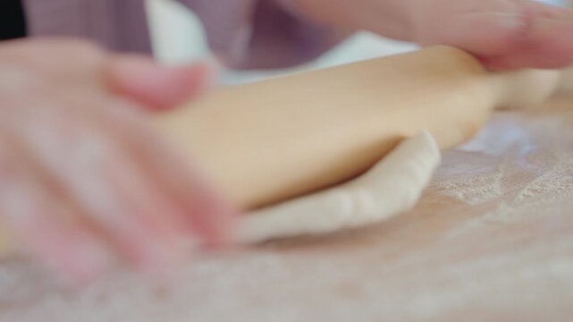 Dough ball rolled with wooden rolling pin in an open kitchen. Pizza and bread on top of counter top and flour