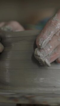 Close-up of potter's hands creating pot from clay concentrated on manufacturing ceramics using pottery wheel. Creative occupation and handmade goods concept.