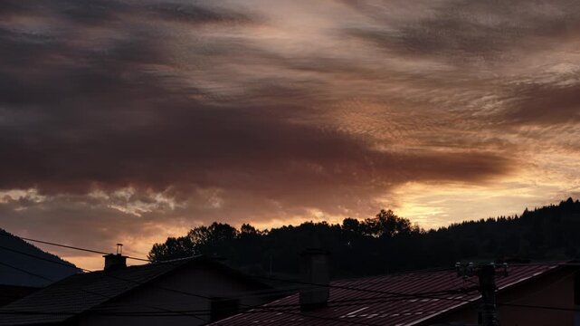 Time Lapse Of Dramatic SunriseClouds Moving Over Village House Roofs And Silhouetted Hills