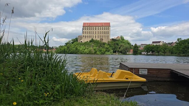 Yellow pedal boats docked at pier with Plumlov Castle across lake