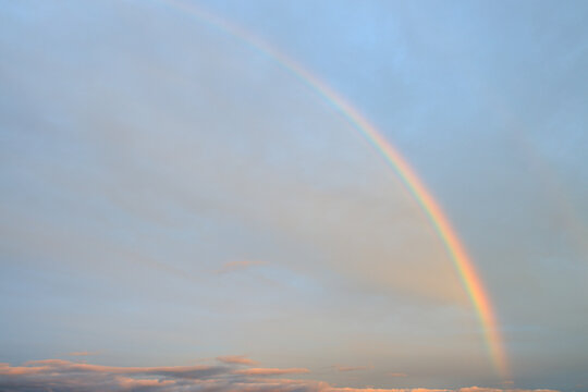 Evening rainbow arching over gentle clouds, atmospheric sky scene