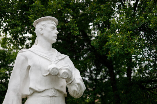 White statue of a sailor with binoculars against green foliage