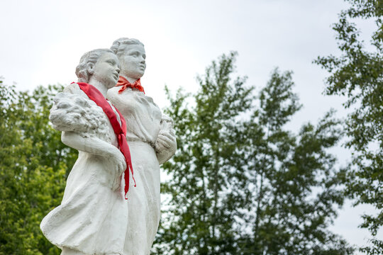 White statue of two young women with red ties in a park