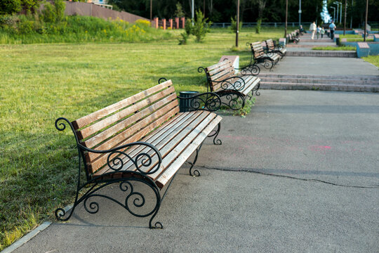 Row of wooden park benches along a paved walkway in a green summer park