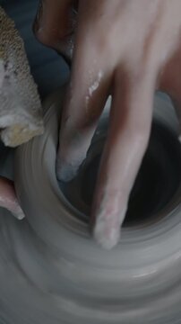 Close-up of child's hands creating pot working with clay on turning wheel in workshop while boy learning pottery. Childhood and crafts concept.