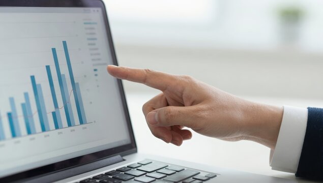Finger pointing at a rising blue bar chart on a laptop screen in a bright office
