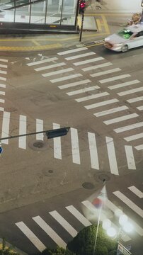 Taxi cars maneuver through a bustling city intersection at night with a pedestrian waiting at the crosswalk. Time-lapse, Seoul, South Korea