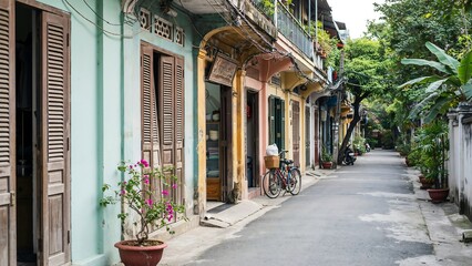 Fototapeta premium Narrow street in an old town with colorful colonial buildings, wooden shutters, potted flowers, and a bicycle parked against a textured wall