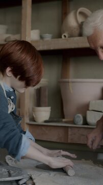 Happy child making artwork from clay learning pottery from skilled grandpa in traditional studio. Creative people and childhood concept.