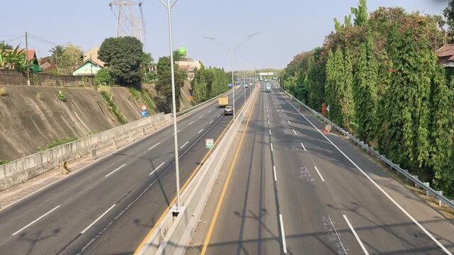 Four-wheeled vehicles traveling along a divided toll road from an elevated view, showing organized highway traffic and modern transportation infrastructure.