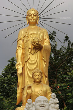 Golden Amitabha Buddha statue with metallic ray halo and small Shakyamuni figurine, traditional zen triad hierarchy composition