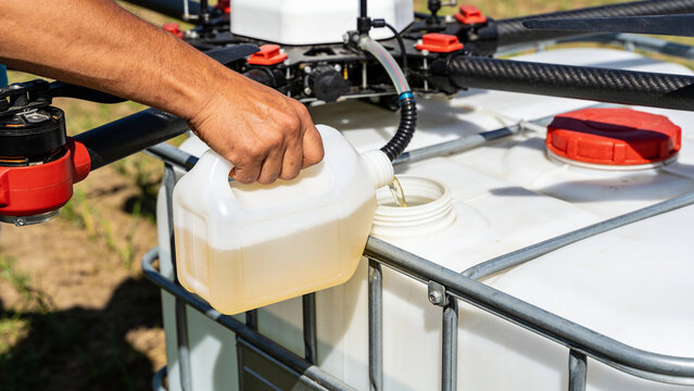Closeup of a hand pouring liquid into a drone sprayer tank for smart farming in agriculture field
