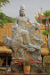 Fototapeta premium Stone Guanyin statue sitting on lunar zodiac rooster mount, traditional Asian astrology cockerel bird sculpture for punctuality and courage