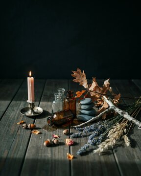 Still life with a pink candle, glass bottles, smooth grey stones, dried lavender, and autumn leaves on a rustic dark wooden table background