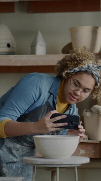 Creative young woman taking photo of handmade ceramic pots in workshop developing small business in social media. Pottery and modern technology concept.