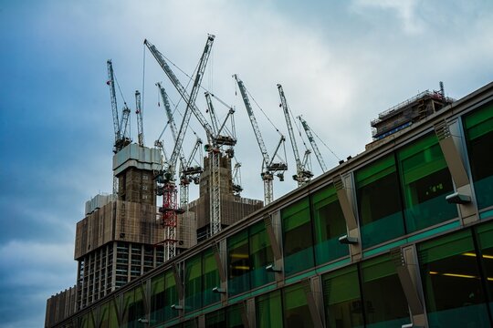 Construction cranes working on skyscraper against cloudy sky