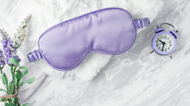 Good night sleep concept, Sleep mask on soft fabric with alarm clock and flower on white marble background, copy space