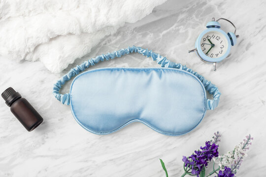 Good night sleep concept, blue sleep mask with alarm clock and essential oil bottle on white marble background