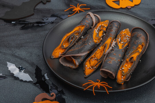 Halloween sweet dessert with traditional decor. Thin black pancakes with pumpkin cream, fall leaves