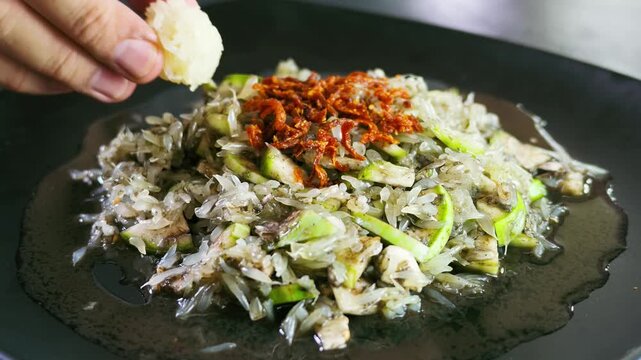 A detailed slow-motion shot showing a hand dipping a small ball of sticky rice into "Tam Som O," a traditional Northern Thai spicy pomelo salad mixed with crab paste.