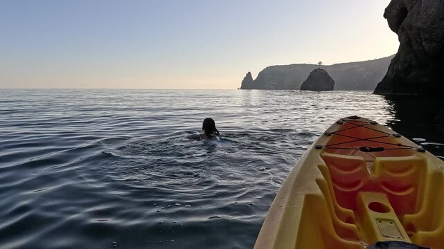Kayaking swimming ocean, woman dives from kayak into calm sea during morning