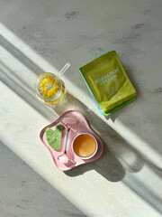 Aesthetic flat lay of green tea sheet mask, jade roller, gua sha, and detox lemon water on a marble surface. Top view composition of a morning wellness and skincare routine  © Jekaterina