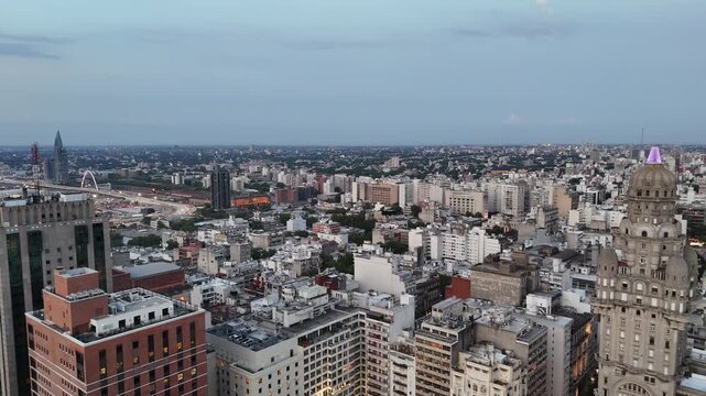 Drone view of Palacio Salvo and Plaza Independencia in central Montevideo at dusk, surrounded by historic and modern buildings with the city skyline extending into the distance.