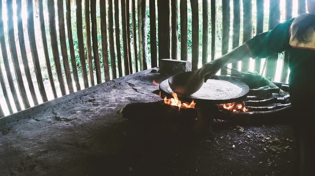 Person Cooking Traditional Flatbread on Hot Pan in Ecuador Amazon House, Firewood Stove, Wooden Interior and Indigenous Food Culture Scene