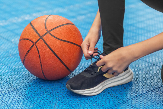 Person tying athletic shoe beside basketball on outdoor court