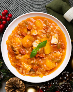 A close-up overhead view of a delicious cod and chorizo stew, garnished with basil, presented with Christmas ornaments