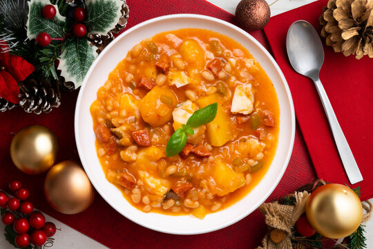 A close-up overhead view of a delicious cod and chorizo stew, garnished with basil, presented with Christmas ornaments