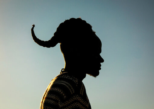 Silhouette of a man with a curved forward-curling hairstyle against the sky at sunset, Cunene Province, Oncocua, Angola