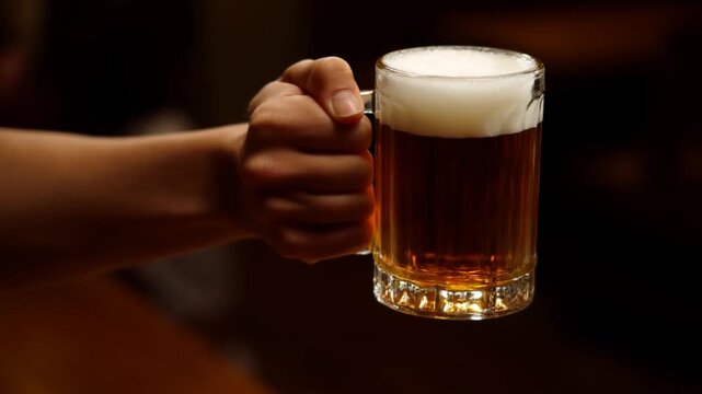 Hand Holding Full Beer Mug with Foam in Dimly Lit Bar Setting