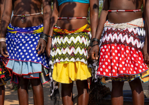 Three women in colorful patterned skirts and beaded belts stand together holding hands, Cunene Province, Cahama, Angola