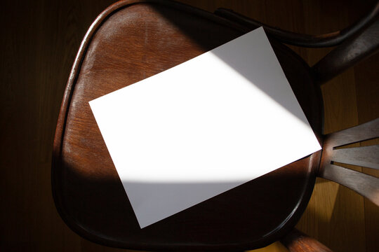 A mockup of a blank sheet of A4 paper on a wooden chair. Soft, diffused focus. A blank poster with space for text, design, and presentation