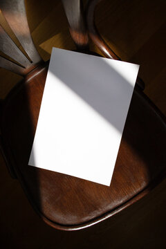 A mockup of a blank sheet of A4 paper on a wooden chair. Soft, diffused focus. A blank poster with space for text, design, and presentation