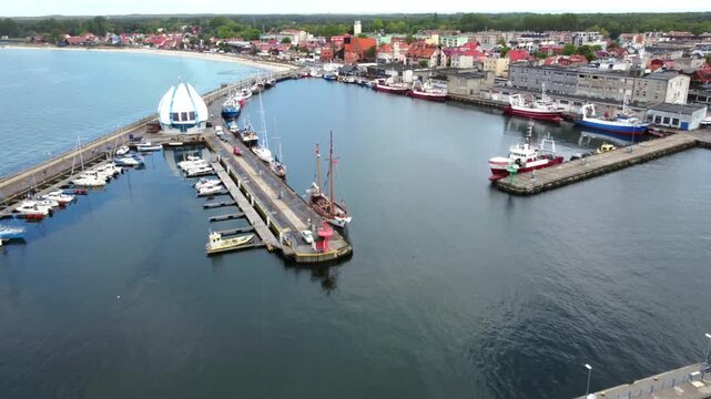Hel Harbour gradually opens into view during a forward flight along the breakwater, revealing the marina, boats and coastal town in Poland.