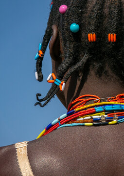 Close-up of braided hair decorated with colorful beads above layered necklaces on a woman's shoulder, Cunene Province, Cahama, Angola