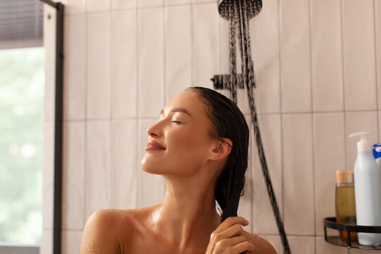Young woman rinsing wet hair under running shower water with eyes closed
