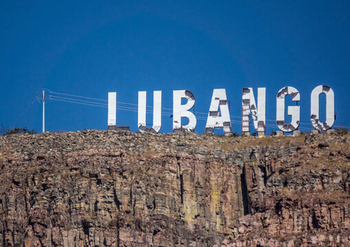 Large white LUBANGO sign standing atop a rocky cliff against a blue sky, Huila Province, Lubango, Angola